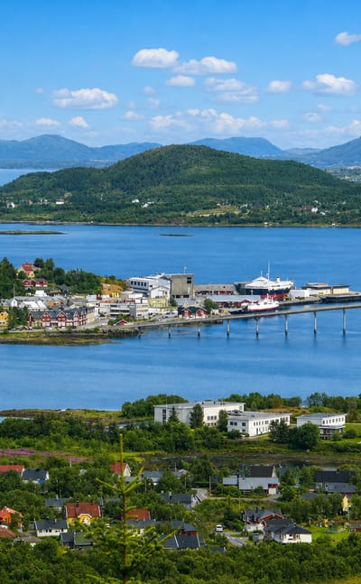 Aerial view of Stokmarknes, Norway, its harbour and bridge spanning the sound amid green islands and mountains.