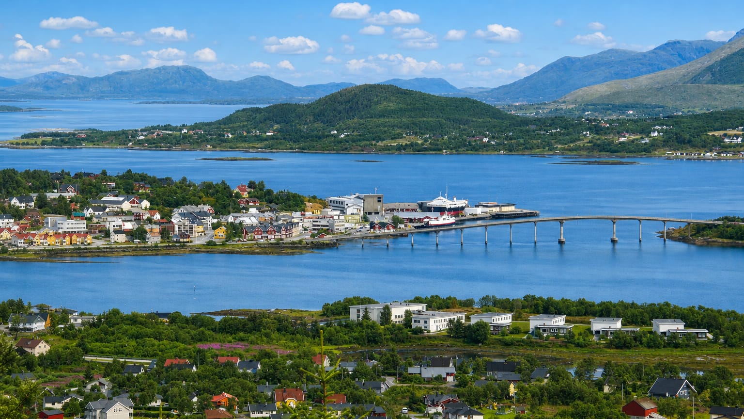 Aerial view of Stokmarknes, Norway, its harbour and bridge spanning the sound amid green islands and mountains.