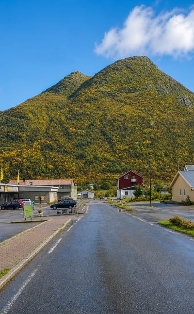 Wet main street of Straume, Norway, with a shop and a distinctive pyramid-shaped hill behind