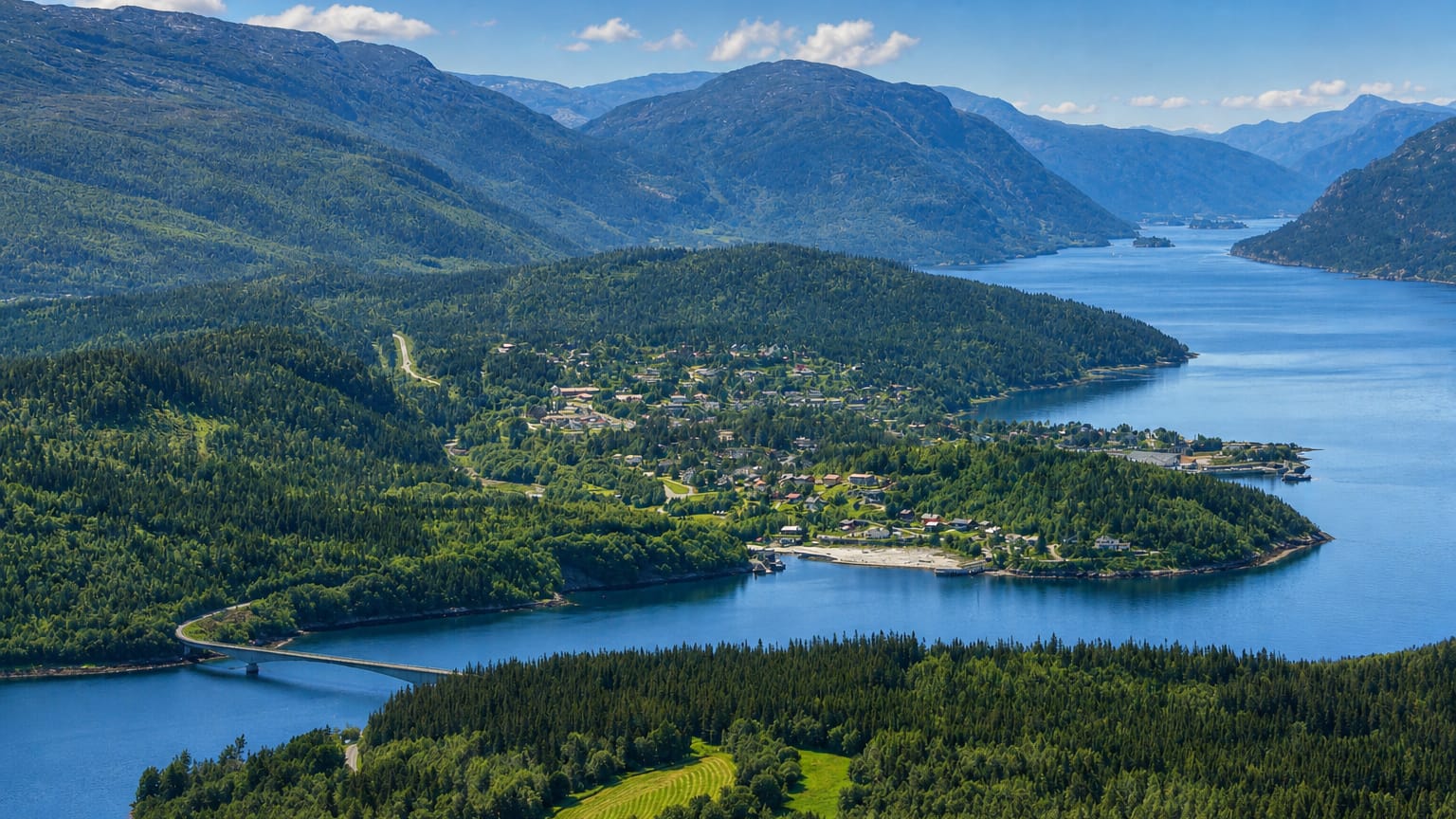 Aerial view of Terråk, Norway, on a forested fjord peninsula with a bridge crossing calm water.