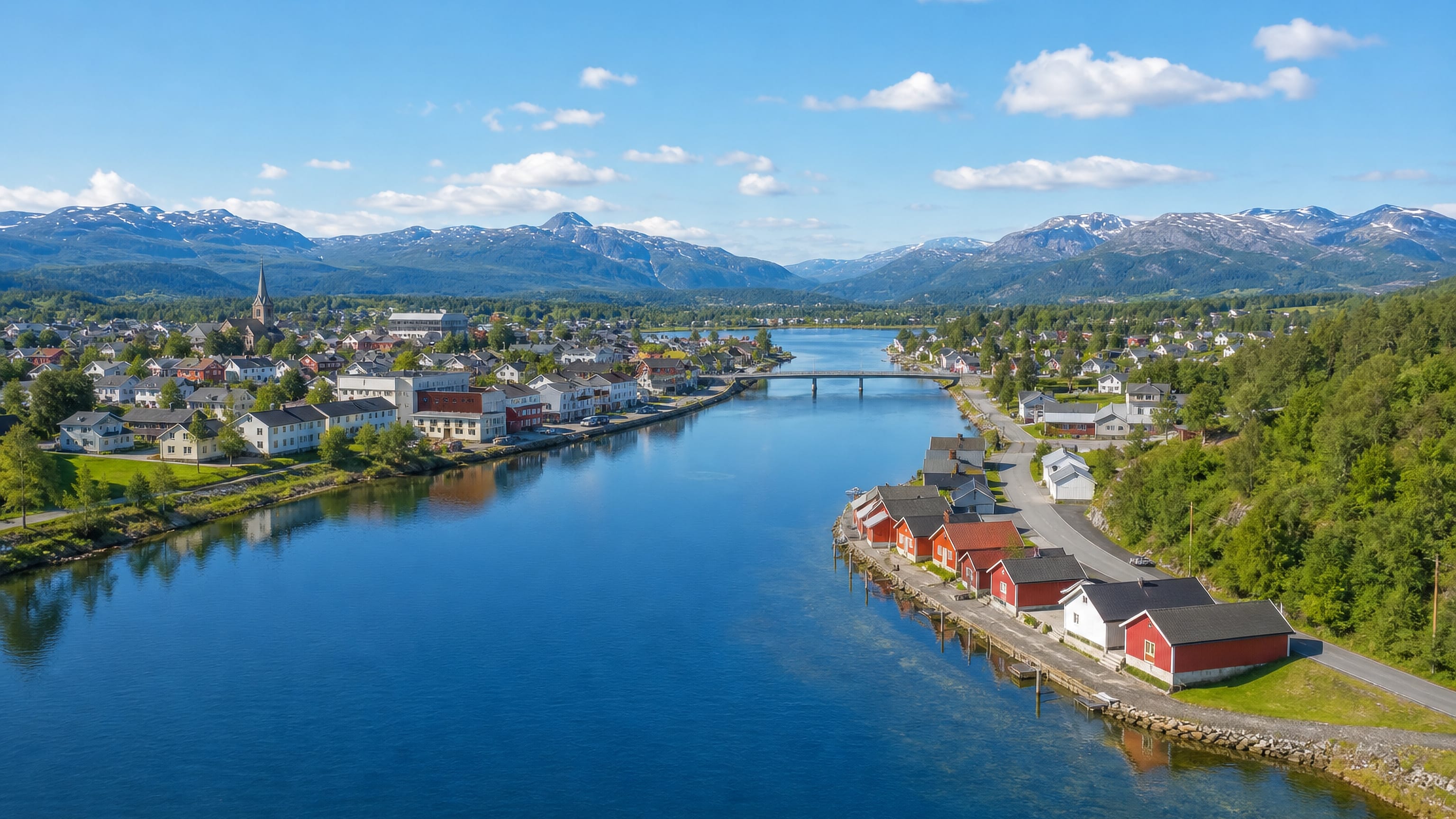 Riverside town of Trofors in Nordland, with red boathouses, a church and snow-capped mountains beyond.