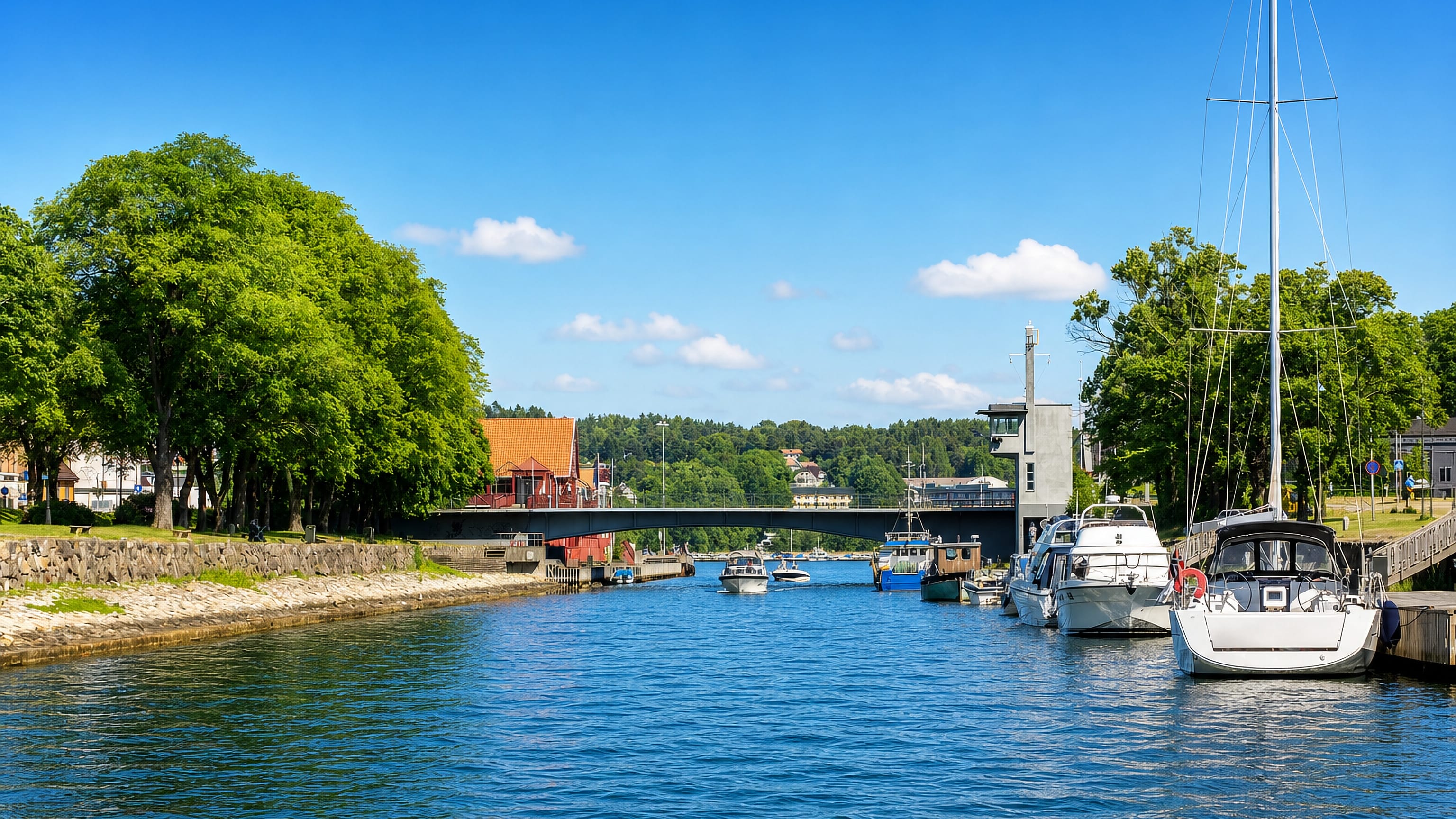 Boats moored along the Moss canal at Mellos, with the bascule bridge and wooded shoreline under a clear summer sky.