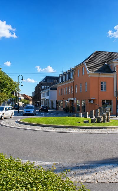 Cobbled roundabout in central Rakkestad, Norway, beside a salmon-pink neoclassical building under a blue sky.