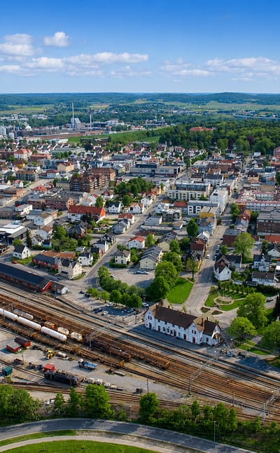 Aerial view over central Sarpsborg, Norway, with rooftops, a rail yard and rolling green countryside.