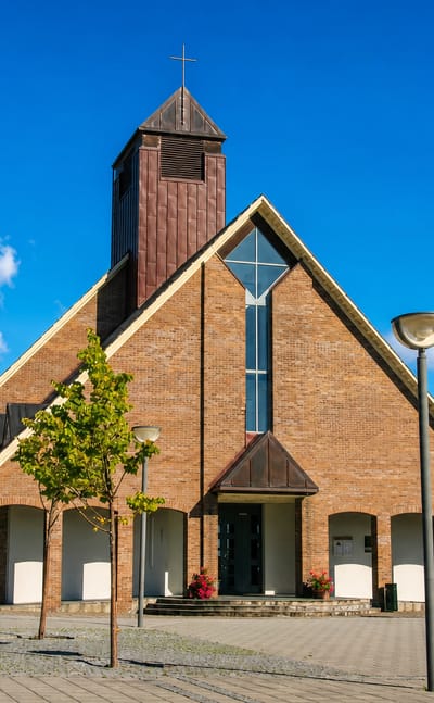 Modern brick church with a wooden bell tower and paved plaza at Aksdal under a clear blue sky