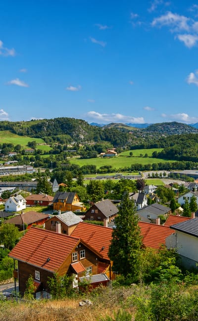 Ålgård nestled in a green valley, red-roofed houses spread below forested hills with a lake and mountains beyond