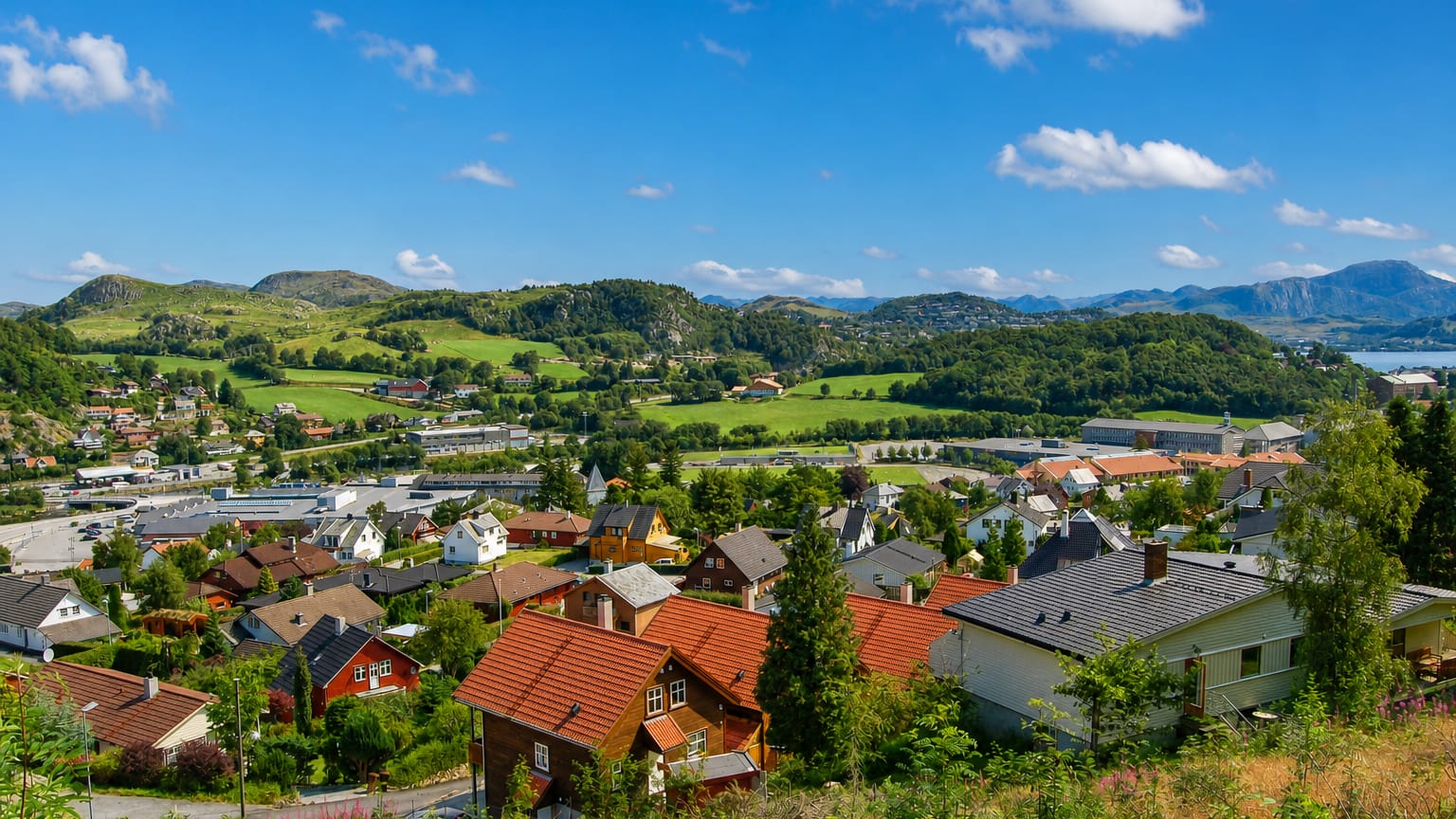Ålgård nestled in a green valley, red-roofed houses spread below forested hills with a lake and mountains beyond