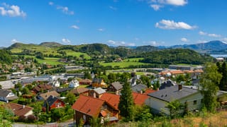 Ålgård nestled in a green valley, red-roofed houses spread below forested hills with a lake and mountains beyond