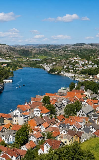 Elevated view over Egersund, Norway, with red-roofed white wooden houses lining the sound, boats and green hills