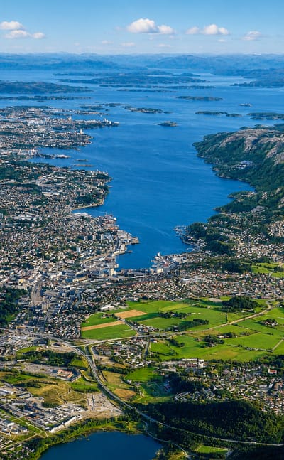 Aerial view of Stavanger spreading along the fjord amid green islands and blue water under scattered clouds