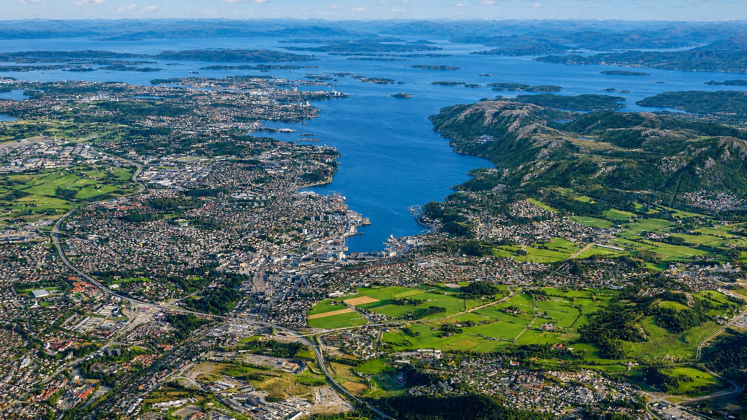 Aerial view of Stavanger spreading along the fjord amid green islands and blue water under scattered clouds