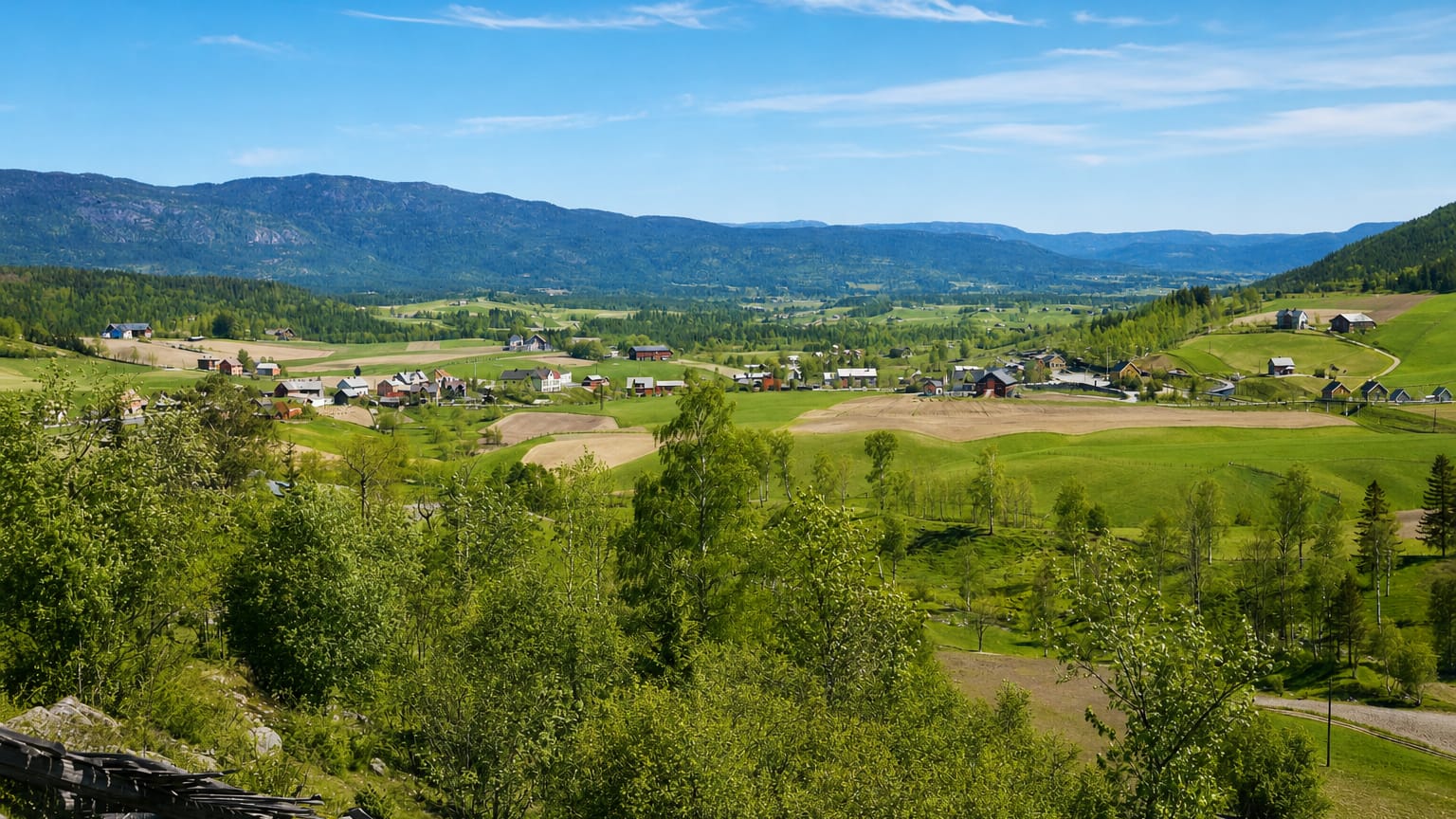 Bø in Telemark across a green valley of scattered farms and fields ringed by forested hills under a blue sky