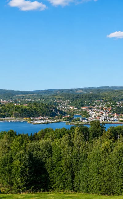 View over Notodden, Norway, beside a lake ringed by forested hills under a blue summer sky