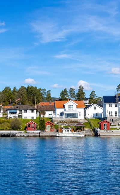 White and red timber houses with boathouses and moored boats along the waterfront at Porsgrunn, Telemark, Norway.