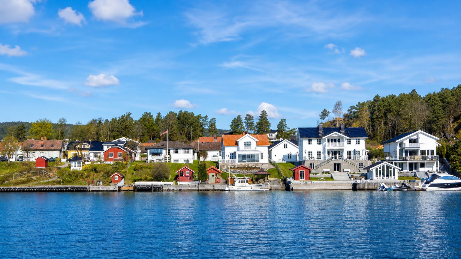 White and red timber houses with boathouses and moored boats along the waterfront at Porsgrunn, Telemark, Norway.