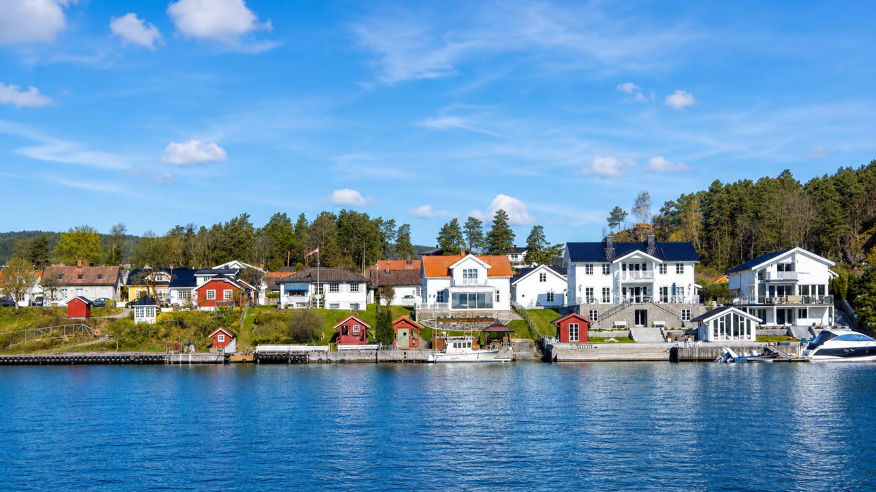 White and red timber houses with boathouses and moored boats along the waterfront at Porsgrunn, Telemark, Norway.