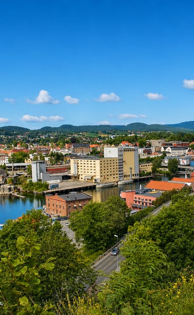 Riverside townscape of Skien with waterway, bridges and a church spire beneath green hills in Telemark