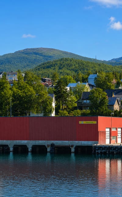 Red boathouse and residential houses on the waterfront below a green mountain at Finnsnes, Norway