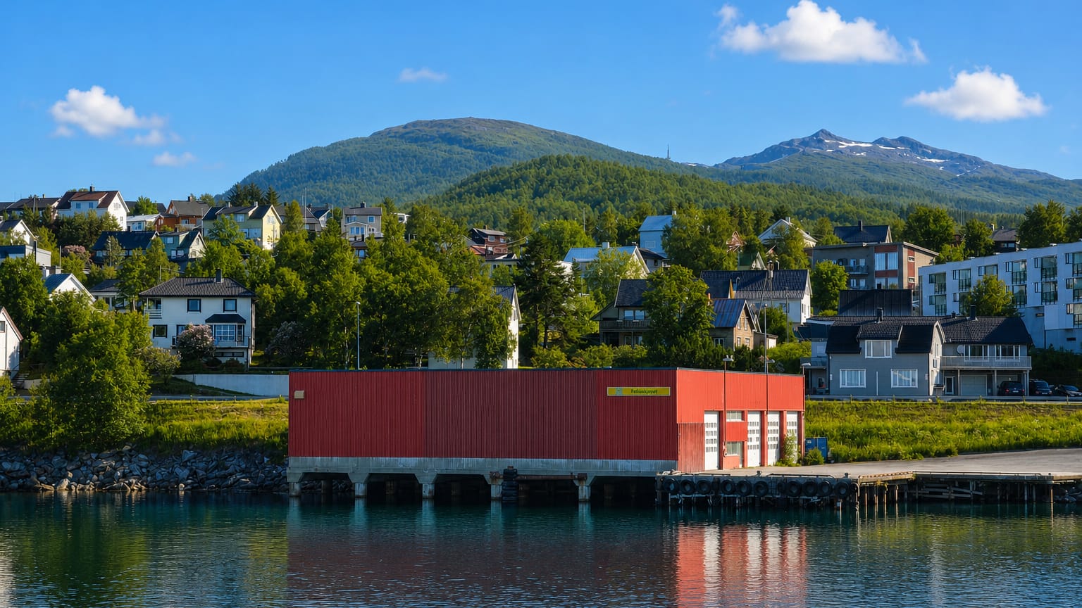 Red boathouse and residential houses on the waterfront below a green mountain at Finnsnes, Norway