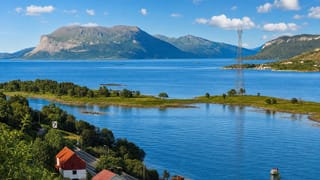 Fjord landscape near Harstad, Norway, with a flat-topped mountain, islets and a power-line pylon.