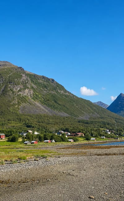 The fjord-side hamlet of Olderdalen in Troms, Norway, spread below a steep green-and-grey mountain on a sunny day.