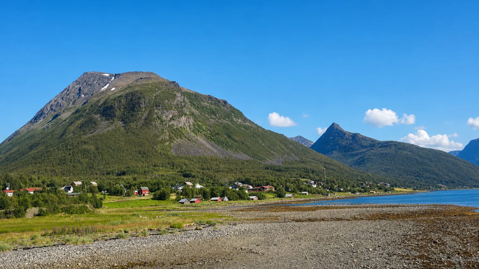 The fjord-side hamlet of Olderdalen in Troms, Norway, spread below a steep green-and-grey mountain on a sunny day.