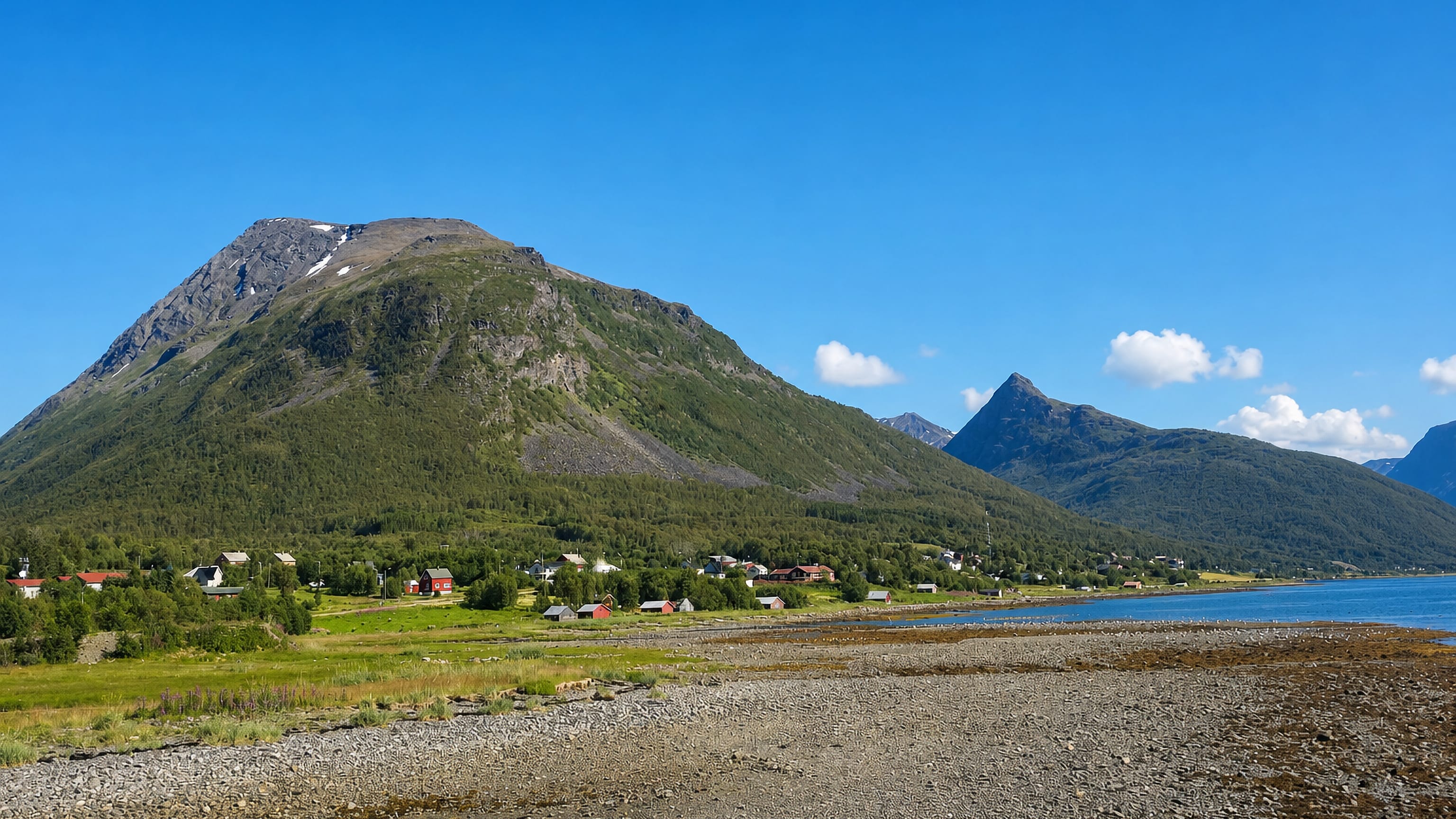 The fjord-side hamlet of Olderdalen in Troms, Norway, spread below a steep green-and-grey mountain on a sunny day.