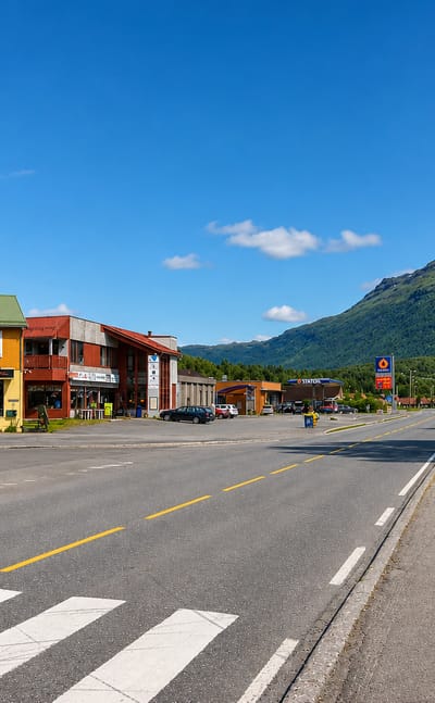 Setermoen's main street with shops, a petrol station and a green mountain rising behind under a blue sky.