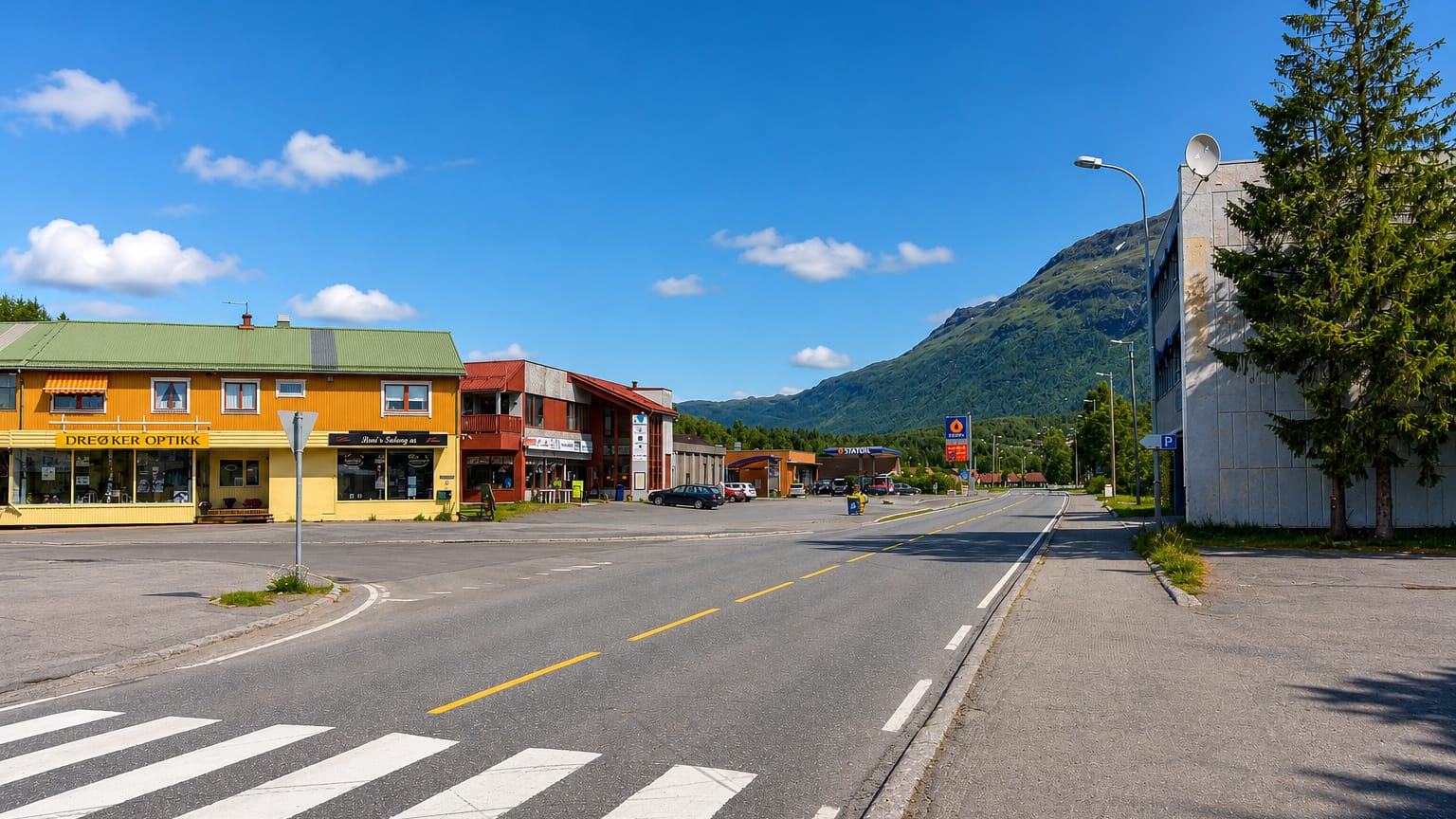 Setermoen's main street with shops, a petrol station and a green mountain rising behind under a blue sky.