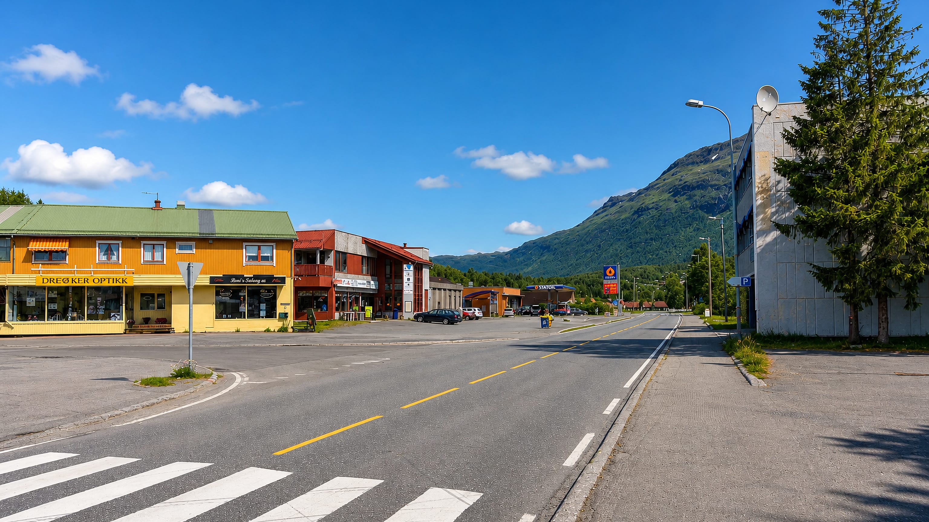 Setermoen's main street with shops, a petrol station and a green mountain rising behind under a blue sky.