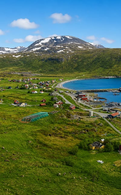 Green coastal settlement with a small harbor breakwater and snow-capped peaks near Skjervoy, Troms, Norway