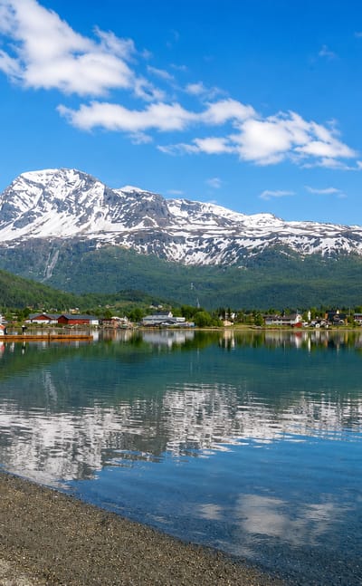 Snow-capped mountain rising above the calm fjord at Tennevoll, Norway, with red houses along the far shore