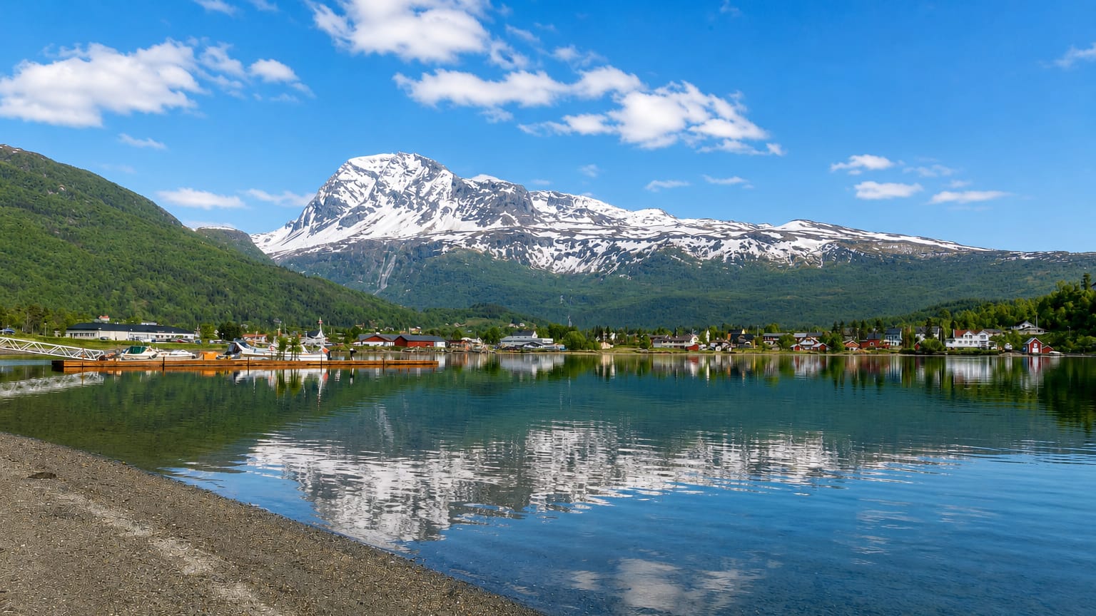Snow-capped mountain rising above the calm fjord at Tennevoll, Norway, with red houses along the far shore