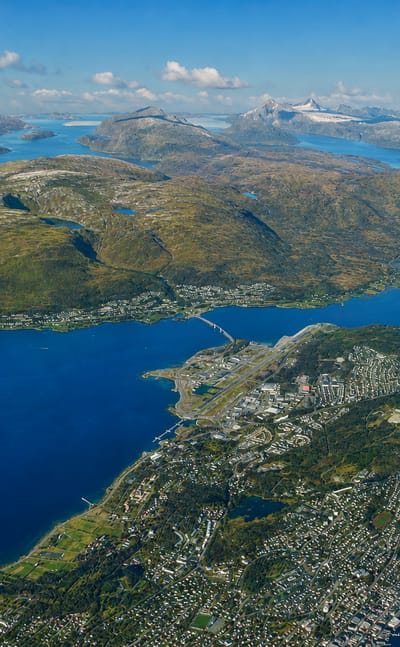 Aerial of Tromso on Tromsoya island with its bridge, airport strip and fjords ringed by snow-capped peaks, Norway.