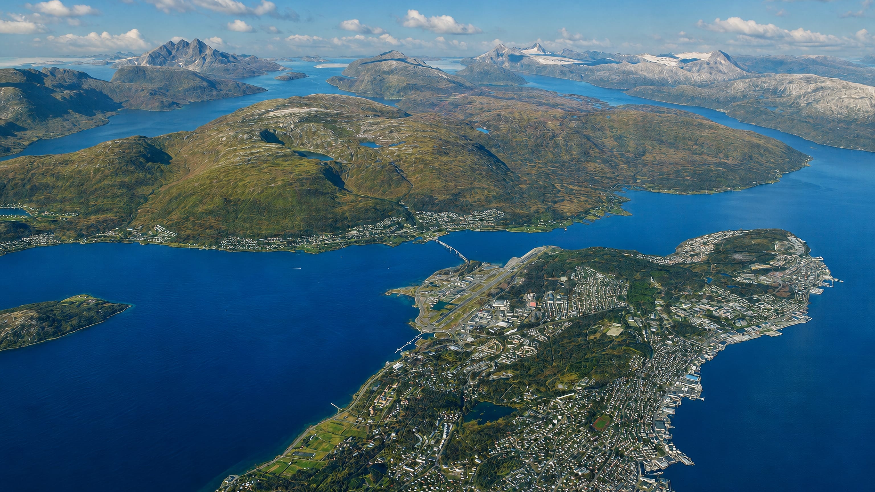 Aerial of Tromso on Tromsoya island with its bridge, airport strip and fjords ringed by snow-capped peaks, Norway.