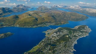 Aerial of Tromso on Tromsoya island with its bridge, airport strip and fjords ringed by snow-capped peaks, Norway.