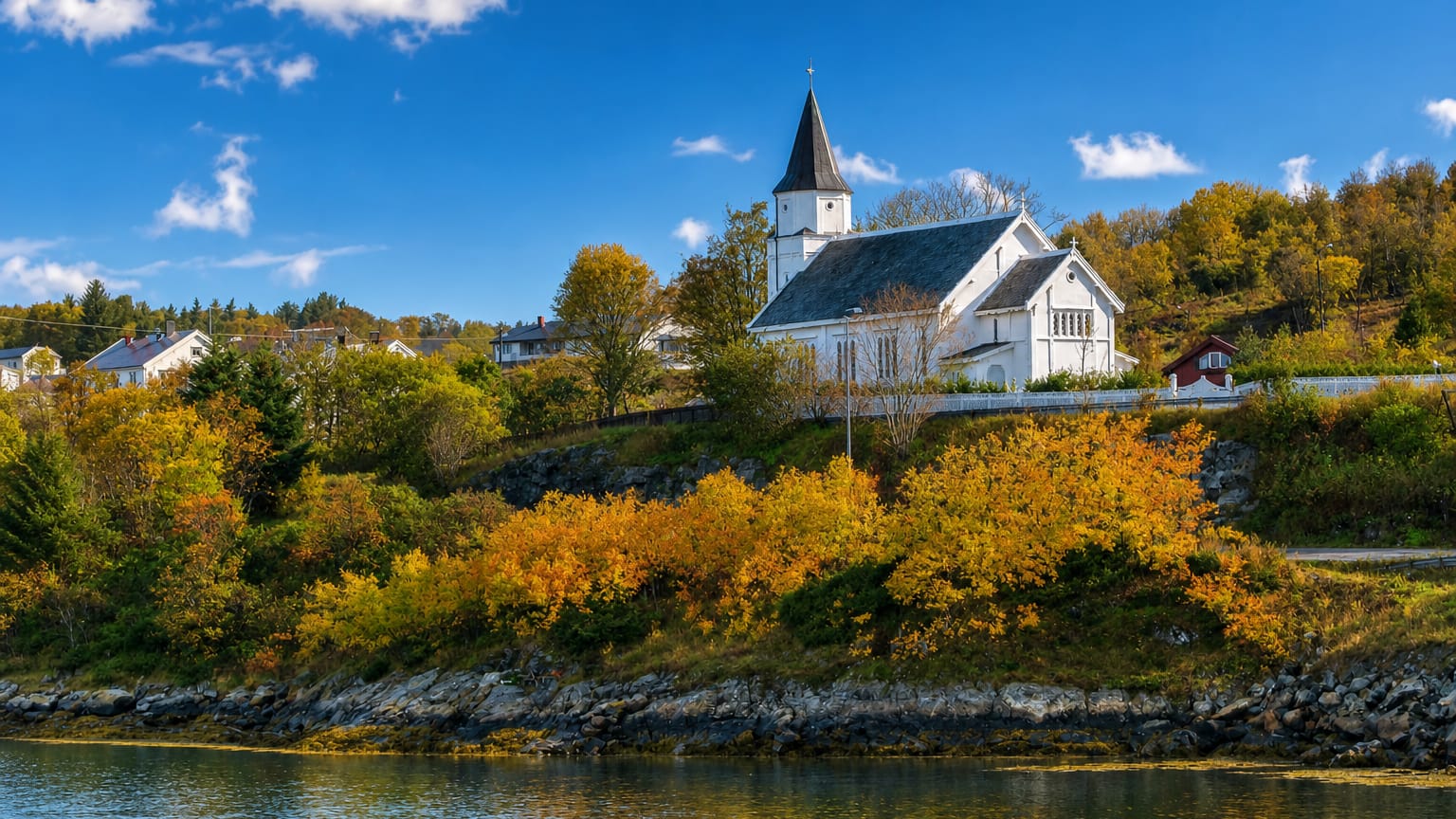 Fillan's white wooden hilltop church above the fjord, framed by autumn foliage and a rocky shoreline, Trøndelag, Norway