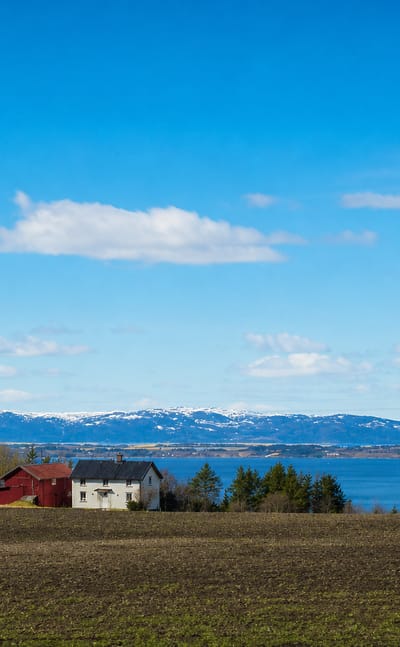 A farm on tilled fields above the fjord with snow-capped mountains at Frosta, Trøndelag, Norway.