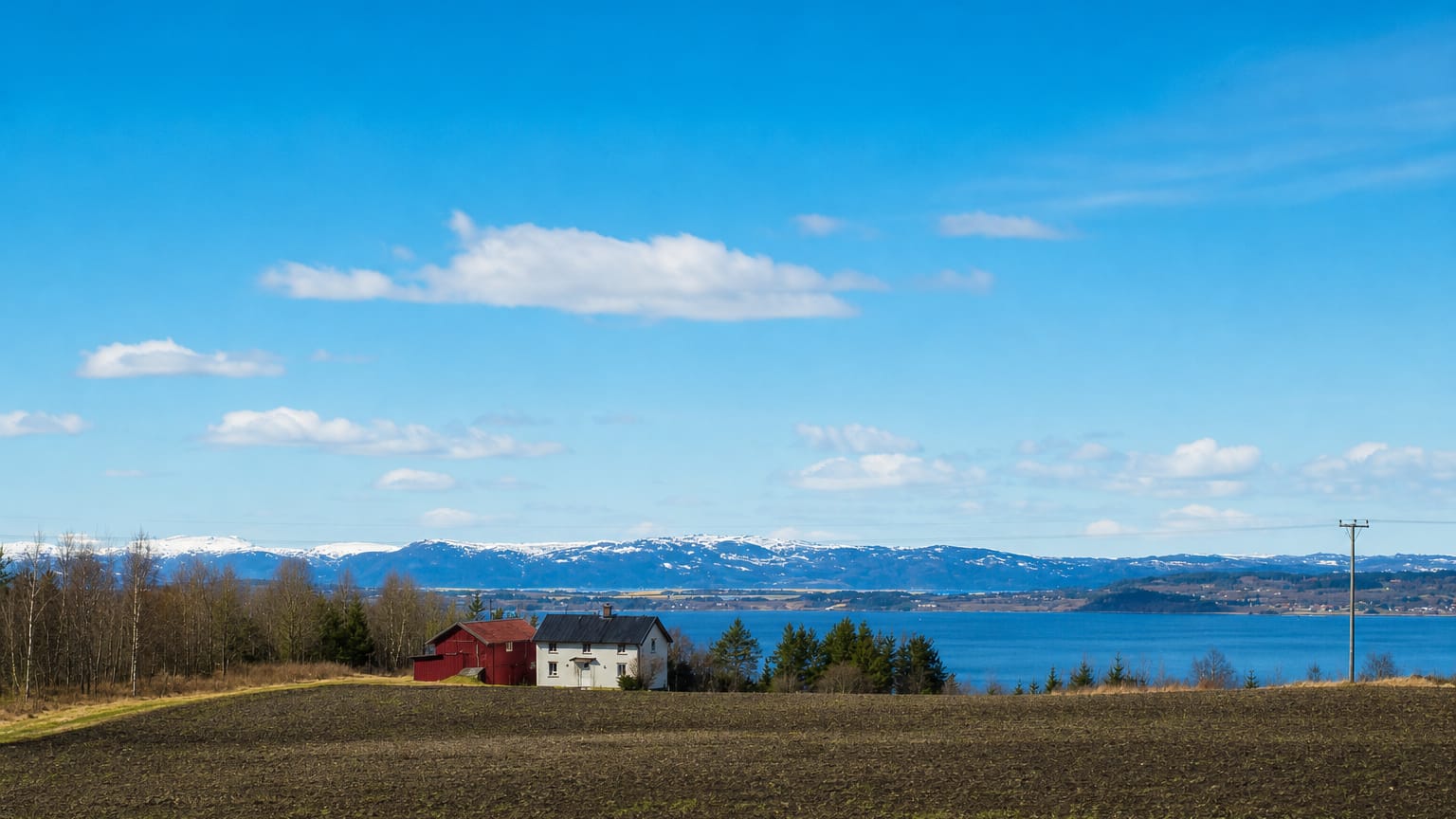 A farm on tilled fields above the fjord with snow-capped mountains at Frosta, Trøndelag, Norway.
