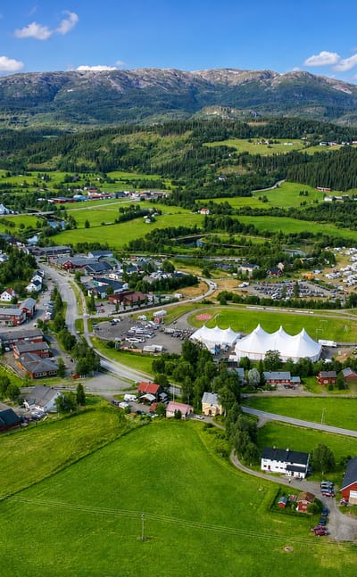 Aerial view of Høylandet village in Trøndelag, Norway, with festival tents and farmland below forested mountains