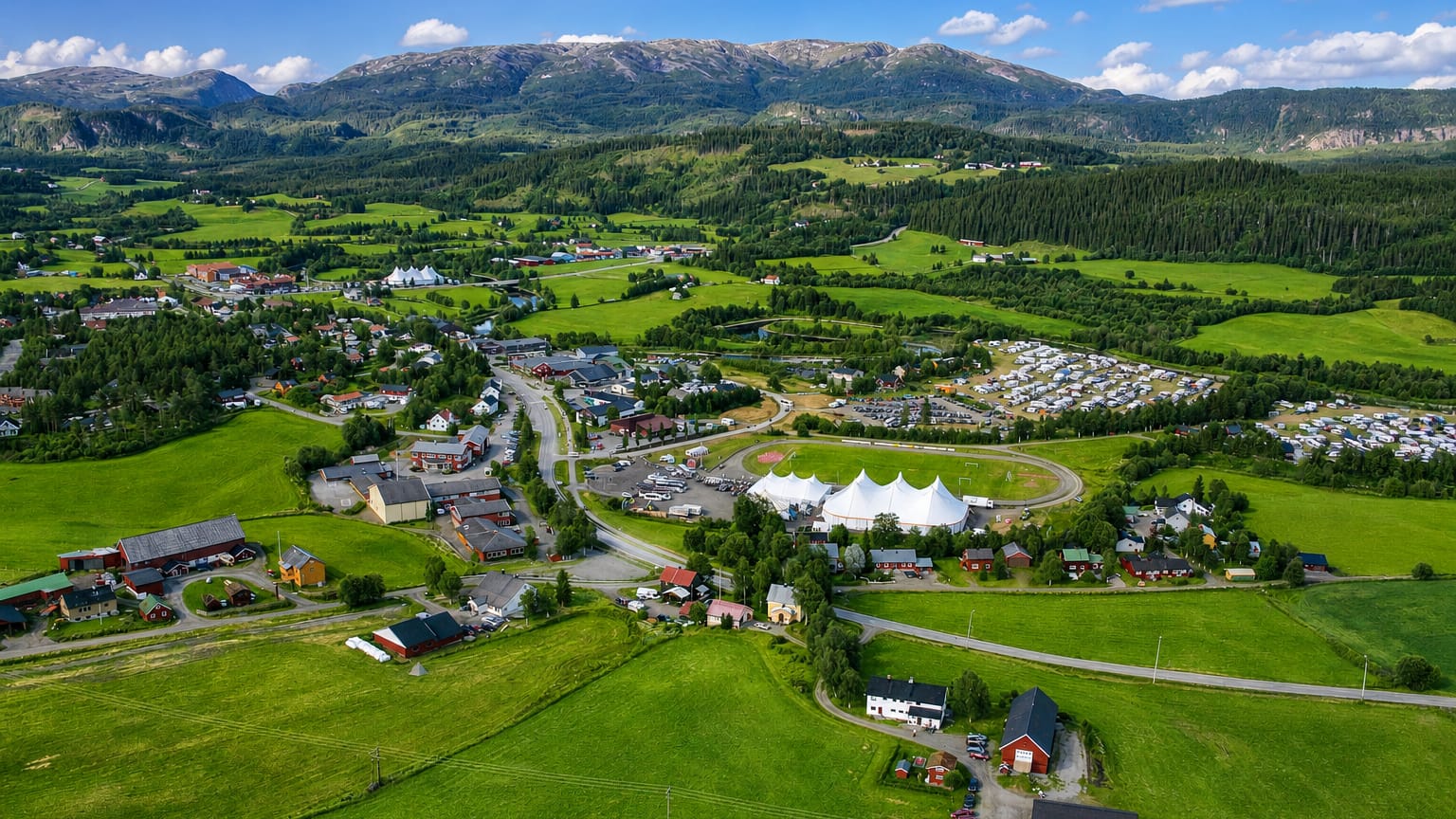 Aerial view of Høylandet village in Trøndelag, Norway, with festival tents and farmland below forested mountains