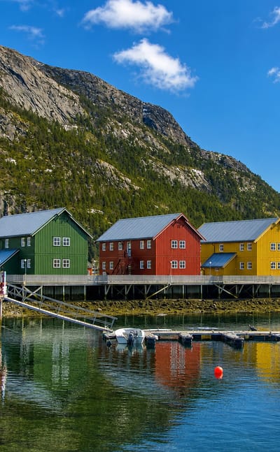 Colorful waterfront houses and a small marina at Lauvsnes, Norway, beneath a steep mountain reflected in calm fjord water.