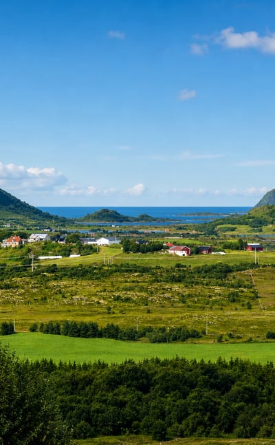 Green farmland and scattered houses between mountains with the sea beyond at Leknes, Norway.