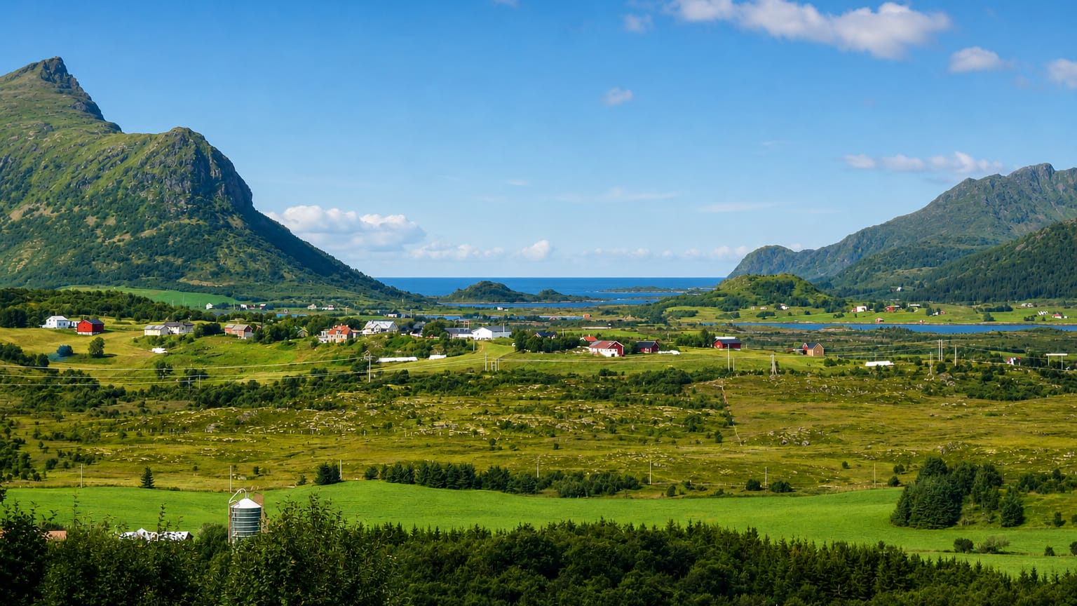 Green farmland and scattered houses between mountains with the sea beyond at Leknes, Norway.