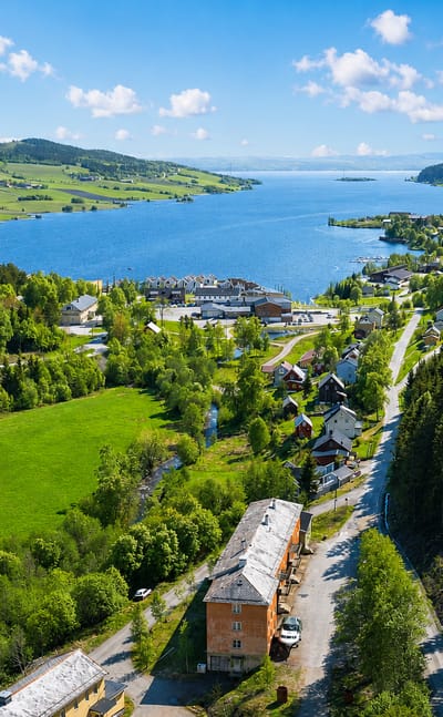 Aerial daytime view of Malm, a small fjord-side town in Trøndelag, Norway, among green hills, meadows and forest.