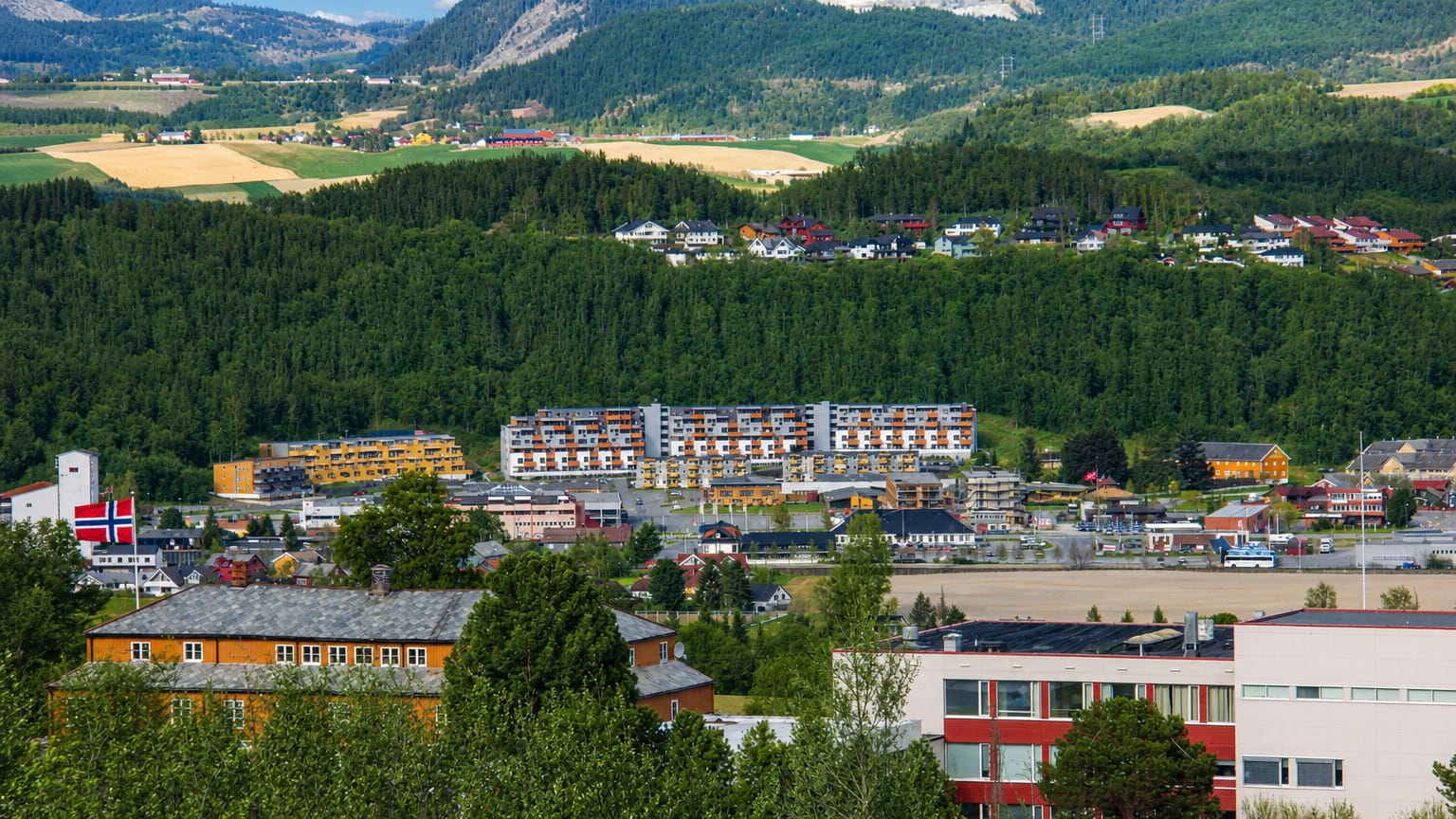 Melhus, Norway, a valley town of low-rise buildings and apartment blocks beneath forested hills and farmland.