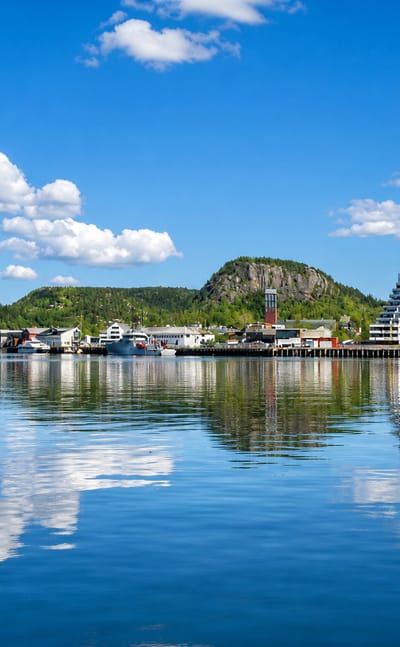 Namsos waterfront with its stepped modern apartment tower and harbour reflected in the calm fjord below forested hills.