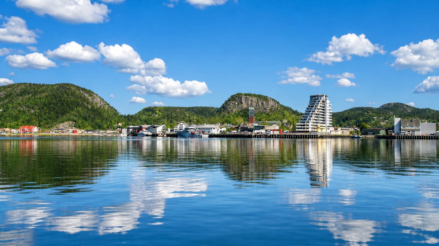 Namsos waterfront with its stepped modern apartment tower and harbour reflected in the calm fjord below forested hills.
