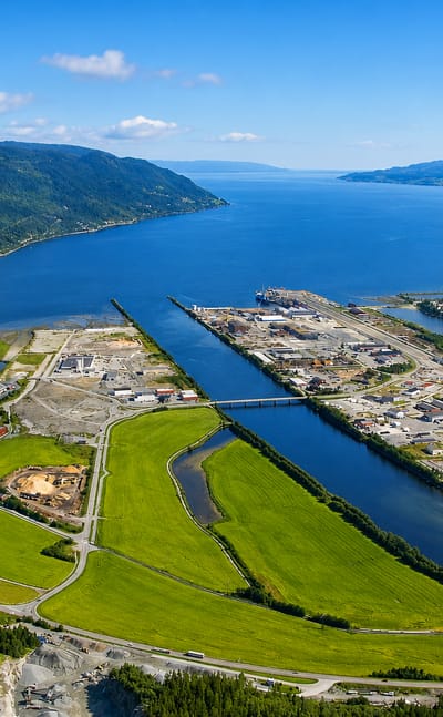 Aerial view of Orkanger at the head of Orkdalsfjord, its industrial harbour and the Orkla river amid green fields.