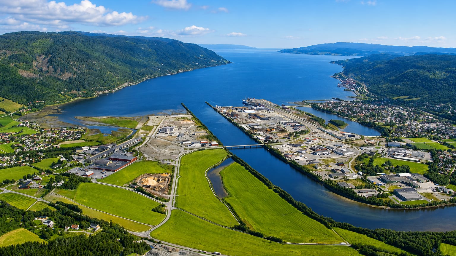 Aerial view of Orkanger at the head of Orkdalsfjord, its industrial harbour and the Orkla river amid green fields.